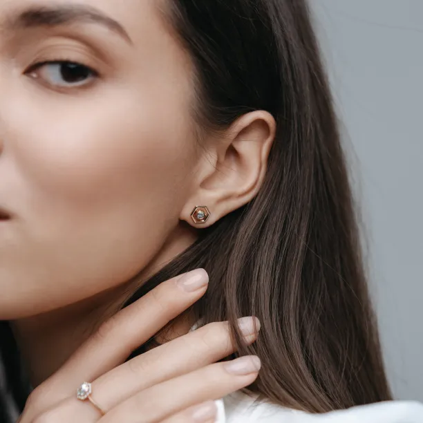 Close-up of a SAM gold hexagonal earring held between fingers