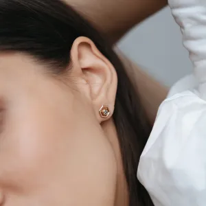 Close-up of a SAM gold hexagonal earring worn on the ear