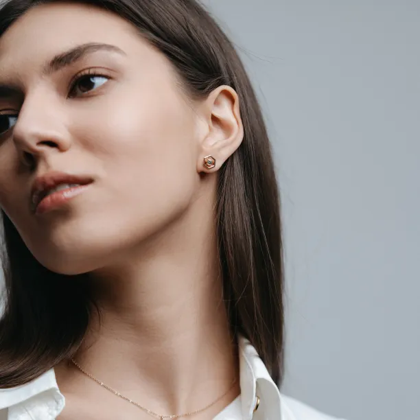 SAM gold hexagonal earring worn on the ear, shown in close-up