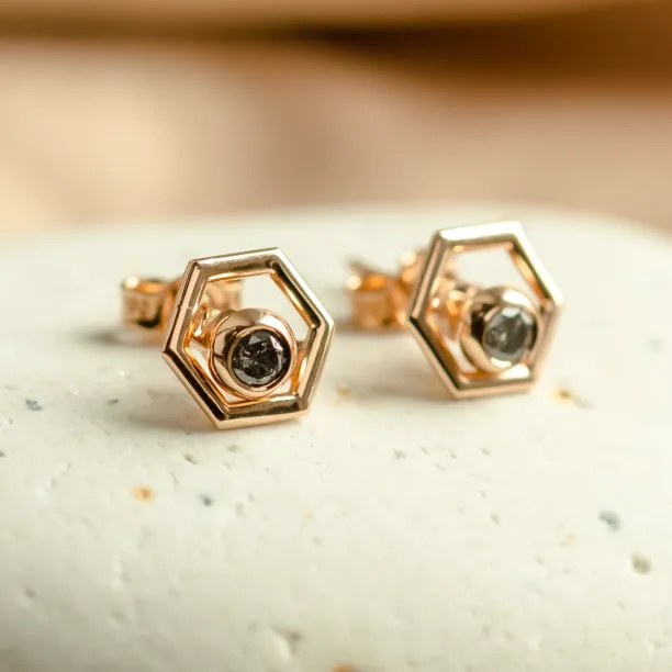 Angled view of SAM gold hexagonal earrings with removable dark gemstones