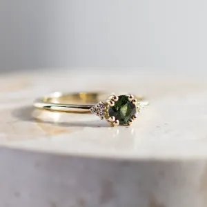 Detailní pohled na zlatý zásnubní prsten se zeleným safírem a diamanty
