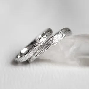 Angled close-up of platinum twig wedding rings with textured surfaces