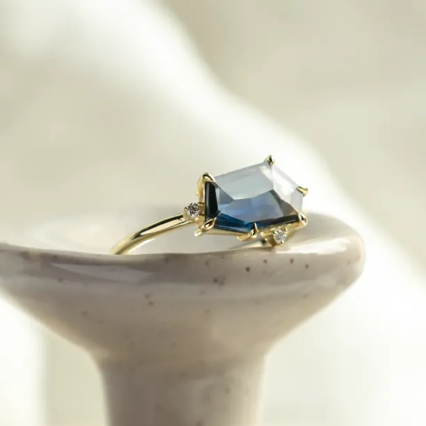 Close-up of the MAGNIFICA gold engagement ring with an asymmetrical teal sapphire and diamonds