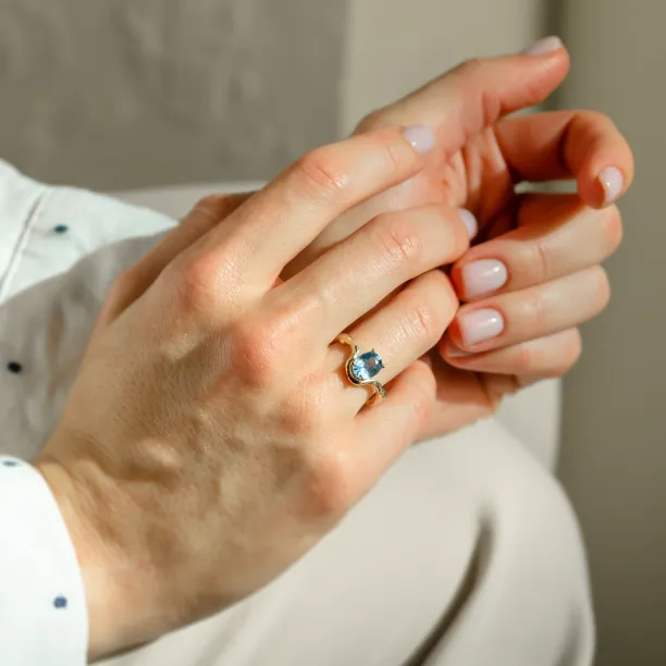 Close-up of KIARA gold ring with oval blue sapphire worn on a hand