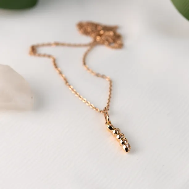 Gold CORINNE necklace laid out with its beaded diamond pendant