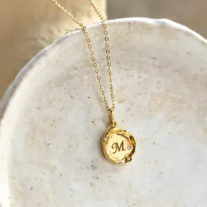 Angled close-up of the COLETTE gold pendant with engraved M and diamond