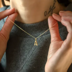 Gold letter A pendant with diamond held against the neck