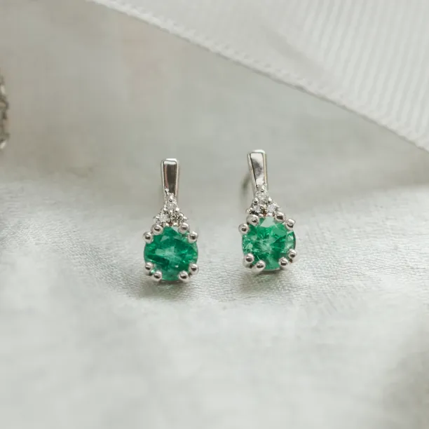 Close-up of paired LENNY gold earrings with emeralds and diamonds