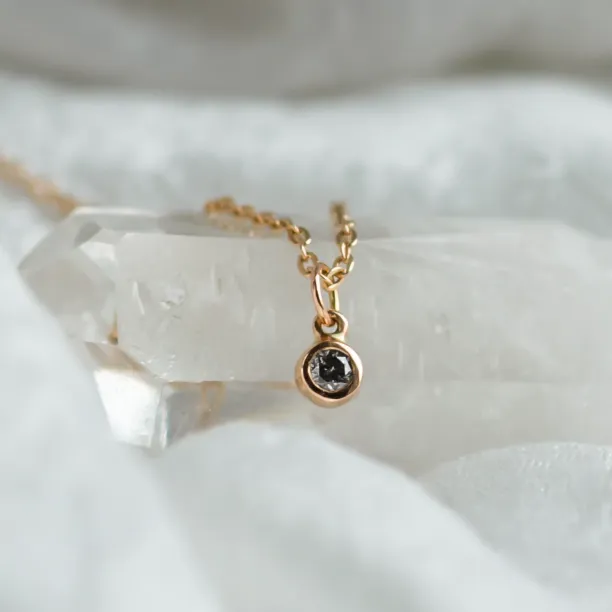 Close-up of the gold pendant with a bezel-set salt and pepper diamond
