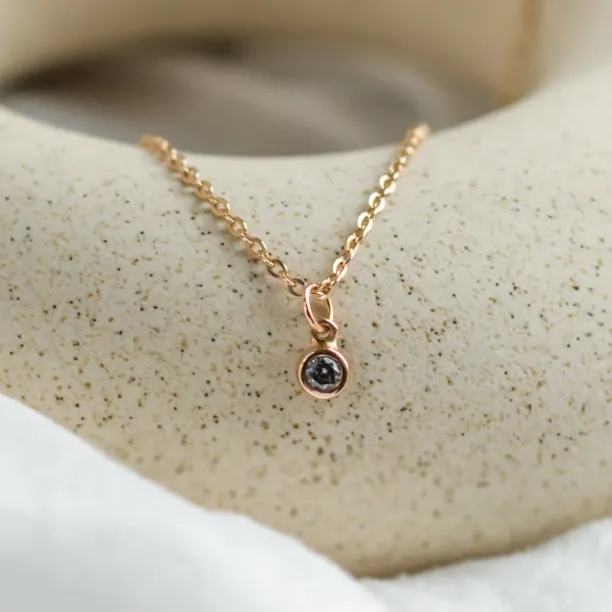 Angled close-up of the gold pendant with a bezel-set salt and pepper diamond