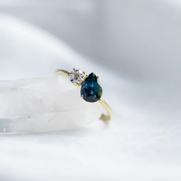 Close-up of the COUPLE ring showing its blue pear sapphire and round diamond