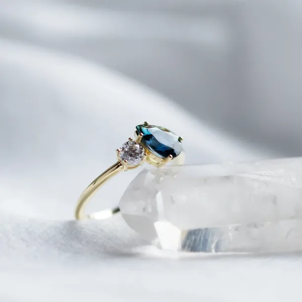 Angled close-up of the COUPLE ring with blue pear sapphire and round diamond