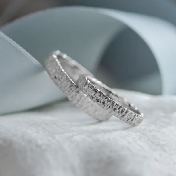 Angled close-up of the unusual texture on BECCA gold wedding rings