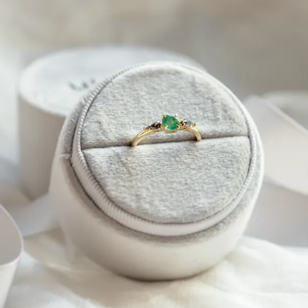 Gold ring with emerald and salt and pepper diamonds shown in an angled view