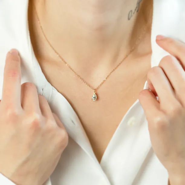 Gold necklace with pear moissanite NAOMI worn on the neck, held by hands