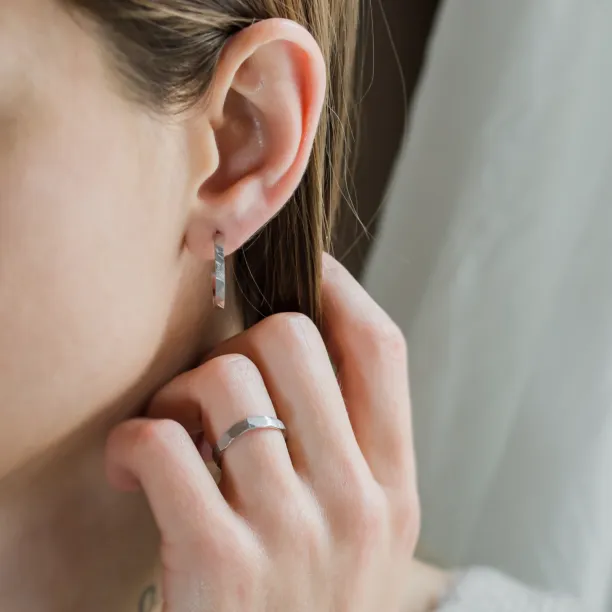 Gold hammered circle earring worn on the ear, with a hand touching the earlobe