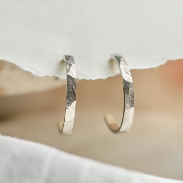 Pair of gold circle earrings with shiny hammered surfaces, angled close-up