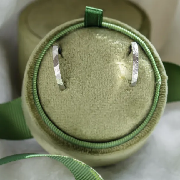 Pair of gold hammered circle earrings displayed on a round jewelry cushion