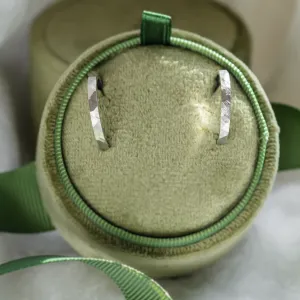 Pair of gold hammered circle earrings displayed on a round jewelry cushion