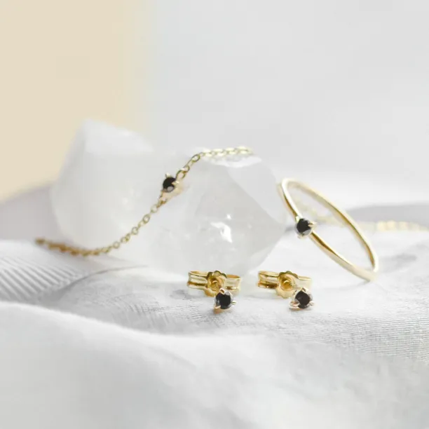 Angled view of the DUNCAN gold jewelry collection with black diamond ring, bracelet and earrings