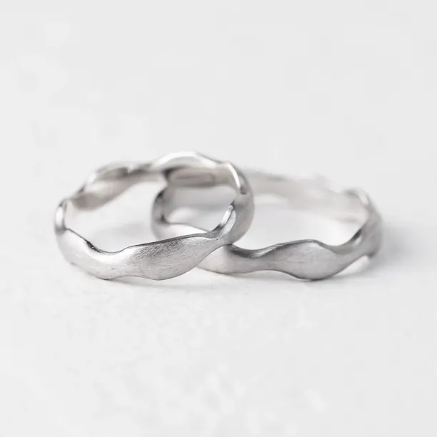 Angled view of the GOCCIO pair of irregular wedding rings