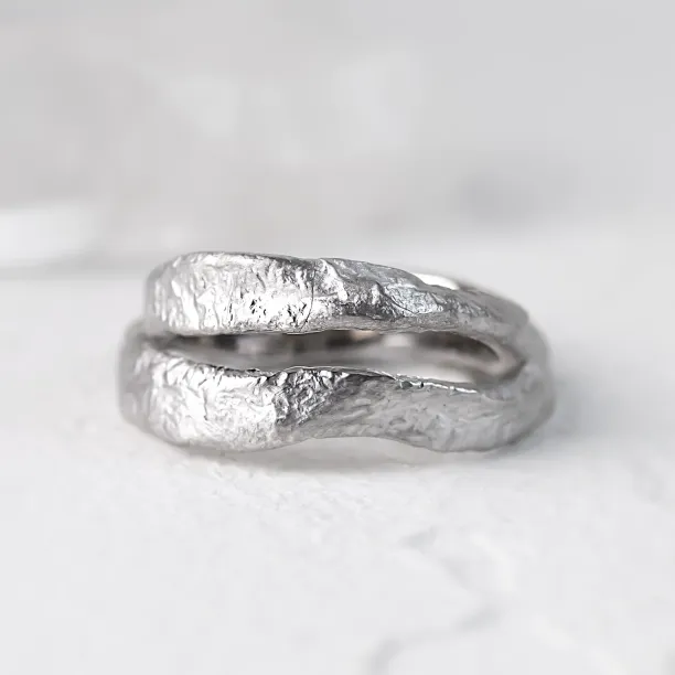 Close-up of stacked MUSK gold wedding bands with irregular moon-surface texture