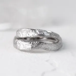 Close-up of stacked MUSK gold wedding bands with irregular moon-surface texture