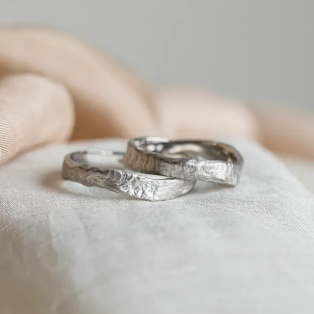 Angled view of overlapping MUSK gold wedding bands with moon-surface texture