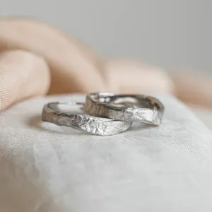 Angled view of overlapping MUSK gold wedding bands with moon-surface texture