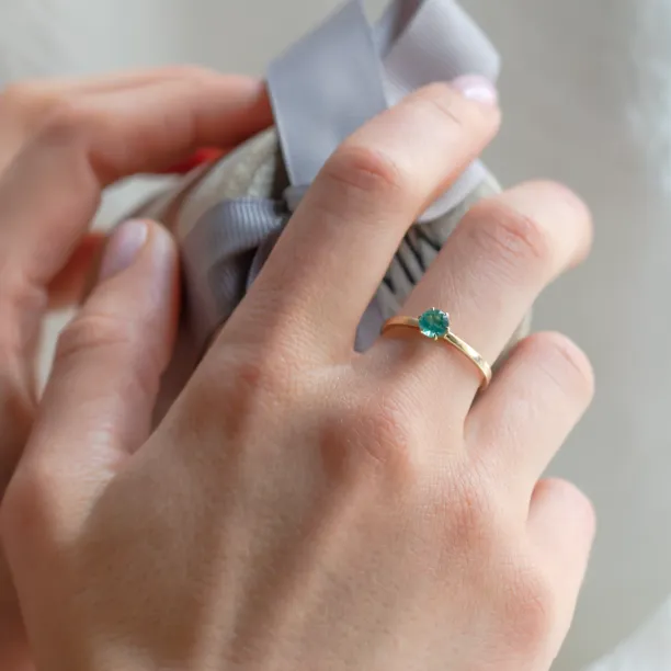 Gold engagement ring with emerald JADE worn on a hand