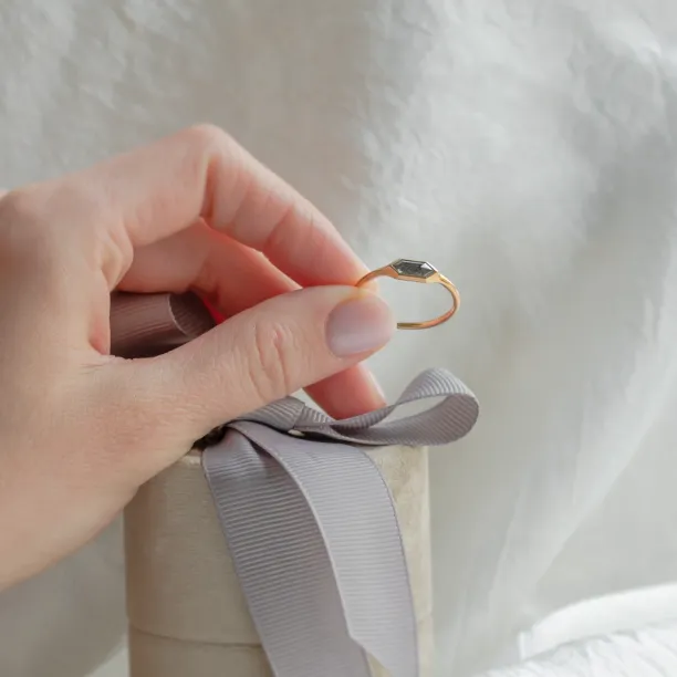 Gold hexagon salt and pepper diamond engagement ring held between fingers