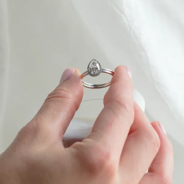 KIMBER pear-shaped moissanite engagement ring held between fingers