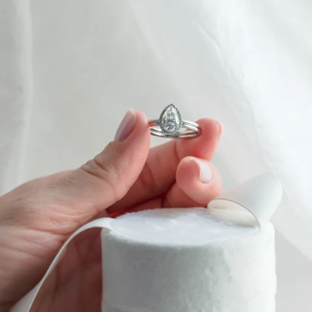 KIMBER engagement set held between fingers, featuring pear-shaped moissanite