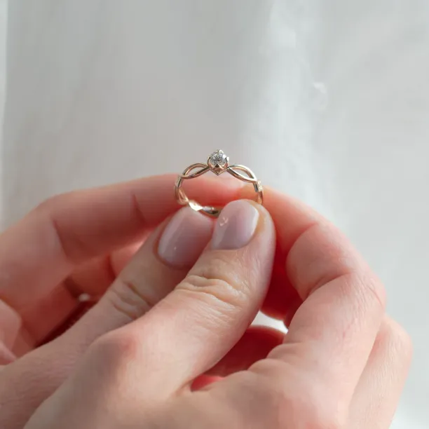 Propletený zlatý prsten QUEENO s lab-grown diamantem držený mezi prsty