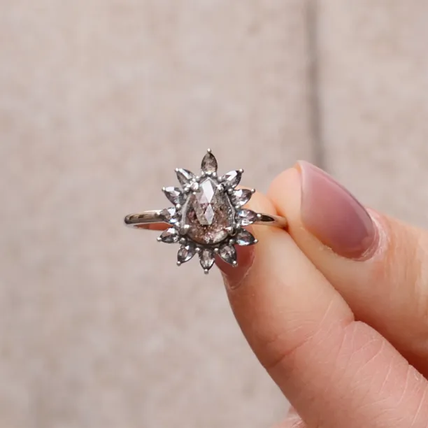Prsten GIRASOLO se salt'n'pepper diamanty ve tvaru květiny držený mezi prsty