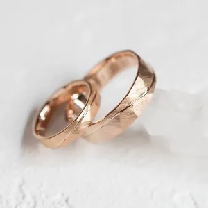 Close-up of LIDO rose gold wedding rings with hammered surface and line