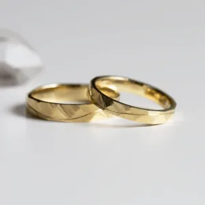 Angled view of LIDO gold wedding rings with hammered surface and line