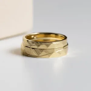 Close-up of overlapping gold wedding rings with hammered surface and line