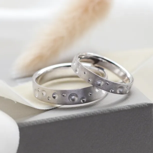 Angled view of SELENE space moon wedding bands with crater-like perforations