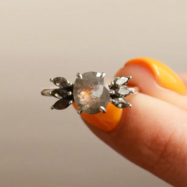 Detail prstenu GIUSTINA se salt'n'pepper diamanty drženého mezi prsty