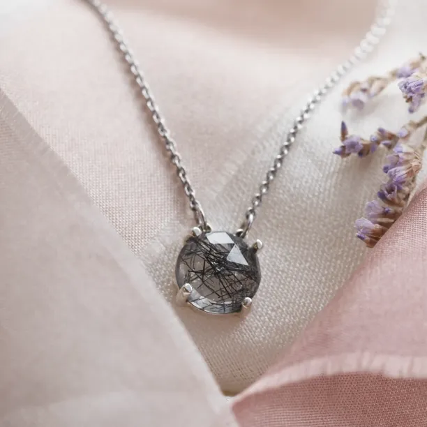 Angled close-up of the MACHA gold necklace pendant with rutile quartz