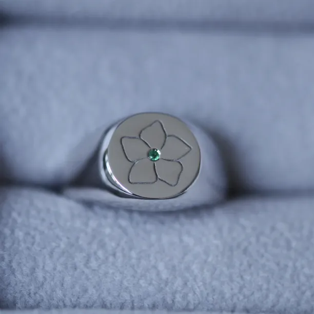 Close-up of the CLARK gold ring's engraved flower and central emerald