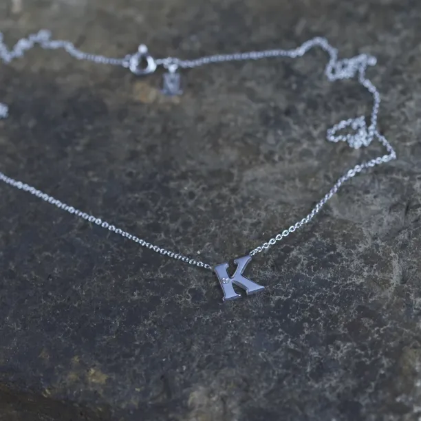 Angled close-up of the VERTE silver letter K diamond pendant