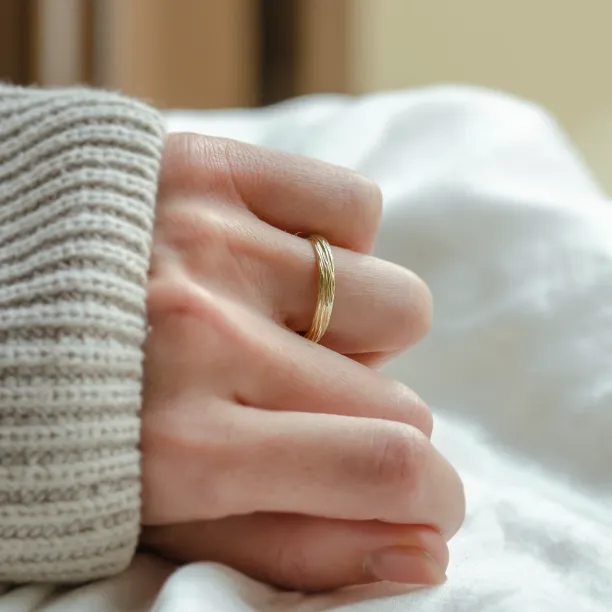 DRIS gold wedding ring worn on a hand, showing its textured band