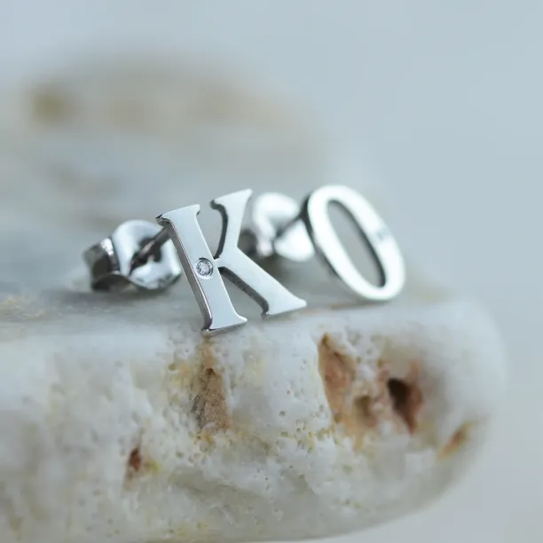 Šikmý detail personalizovaných stříbrných náušnic s diamanty a písmeny