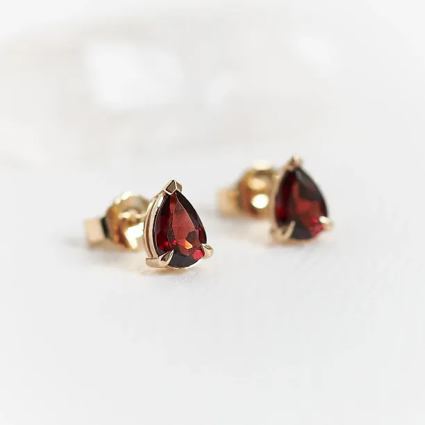 Angled close-up of CARLIE gold earrings with pear-shaped garnets